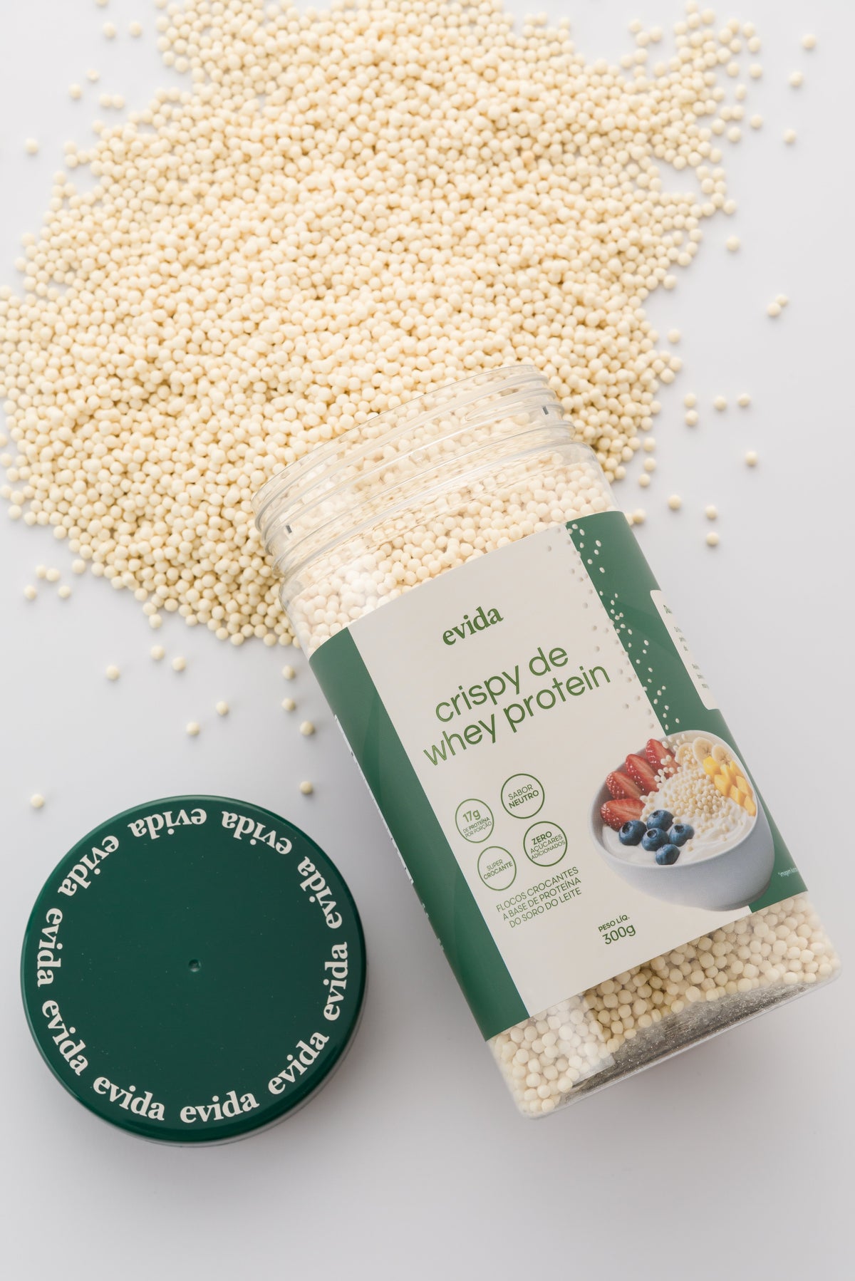 Pote de crispy de whey protein da Evida deitado, com os flocos se espalhando sobre fundo claro