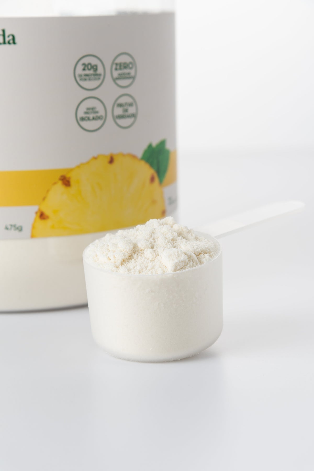 Dosador com whey protein em pó em primeiro plano, com a embalagem do clear whey da Evida desfocada ao fundo