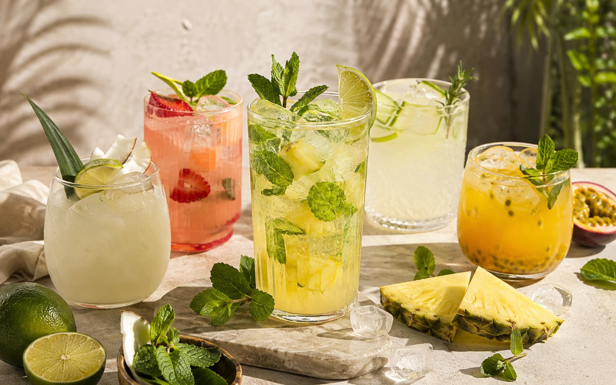 Cinco mocktails sem álcool com clear whey em copos de vidro, com abacaxi, morango, limão, coco e maracujá