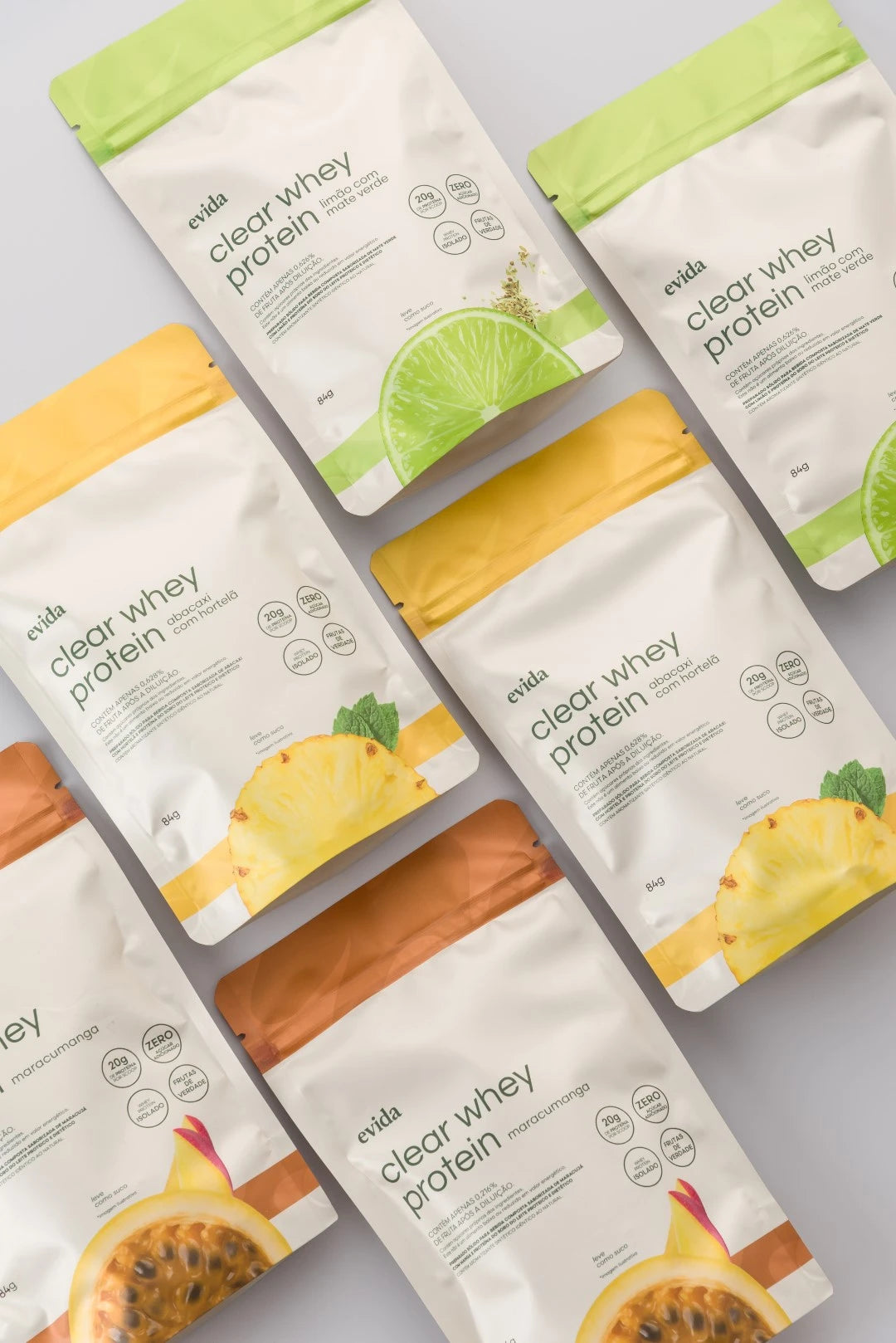 Pacotes de Clear Whey Protein Evida em três sabores com design clean e fundo claro em disposição organizada.